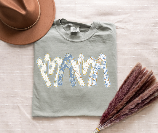 Gray sweatshirt with 'MAMA' text on a light wooden surface with a hat and dried plant.