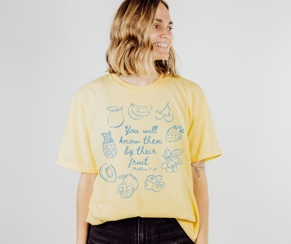 Person wearing a yellow t-shirt with fruit illustrations and text on a plain background
