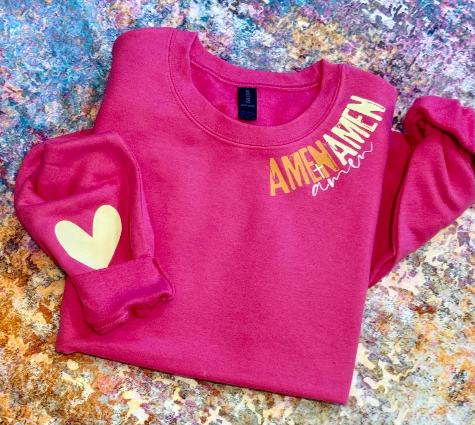 Pink sweatshirt with 'AMEN' text and heart design on a textured surface