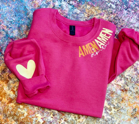 Pink sweatshirt with 'AMEN' text and heart design on a textured surface
