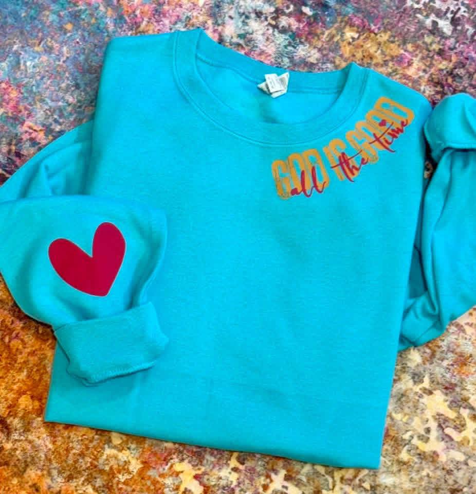 Turquoise sweatshirt with red heart and yellow text on a textured surface
