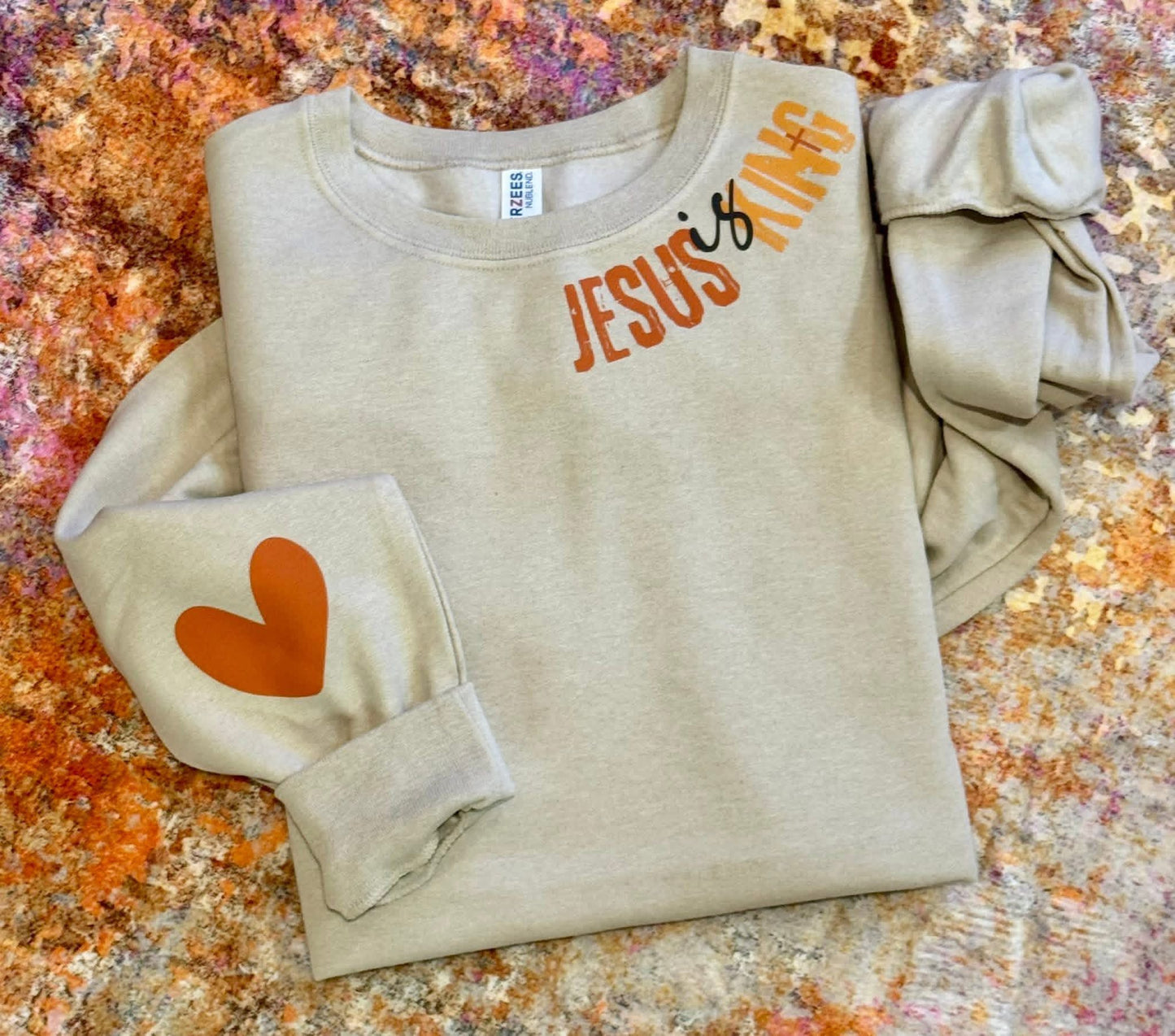 Beige sweatshirt with 'Jesus is King' text and heart design on a textured surface