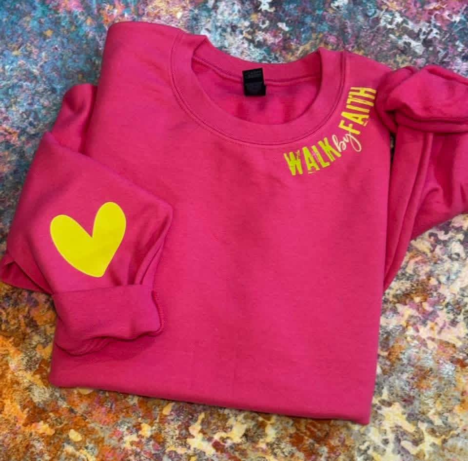 Pink sweatshirt with yellow heart and text on a textured surface