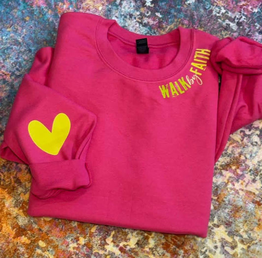 Pink sweatshirt with yellow heart and text on a textured surface